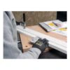 A gloved person using a sanding sheet on a wooden board clamped