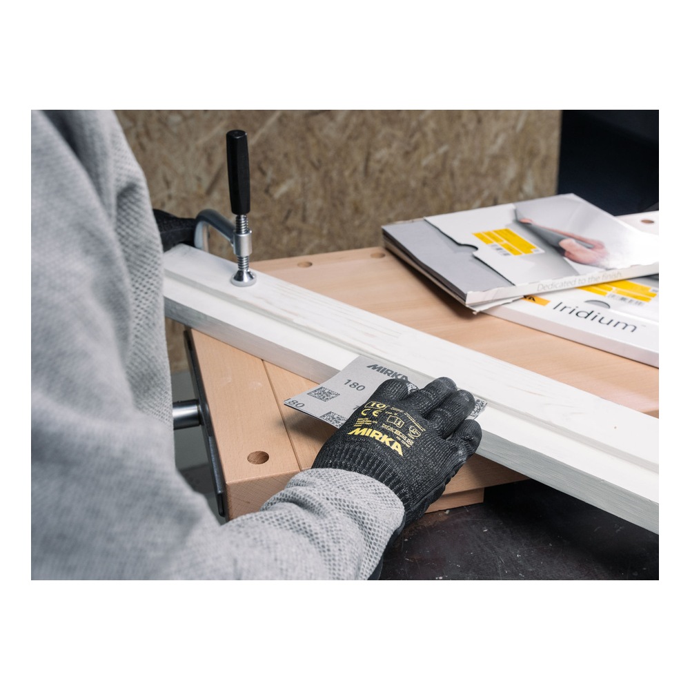 A gloved person using a sanding sheet on a wooden board clamped