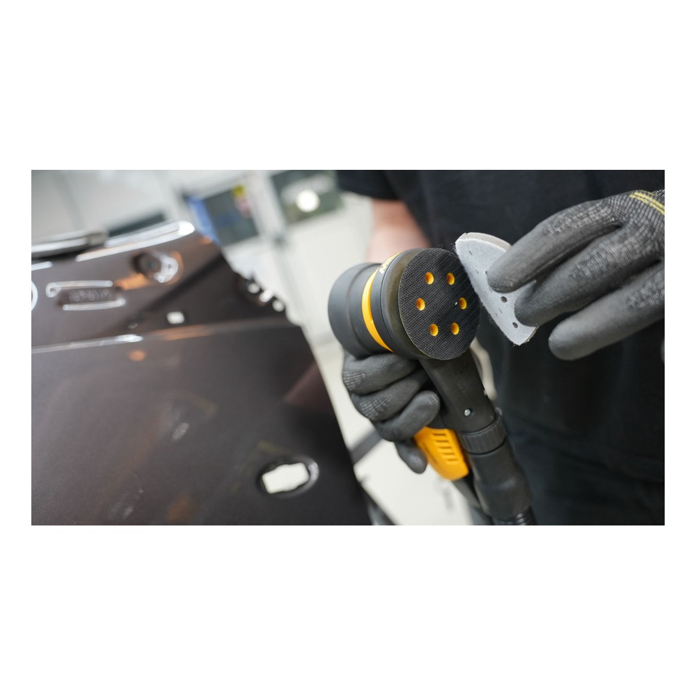 Gloved hand holding sander beside perforated sanding disc