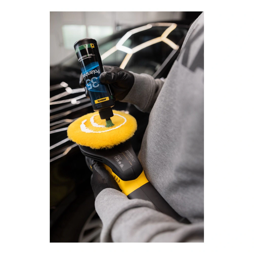 A person wearing gloves uses a polishing machine on a black car surface