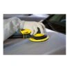 A gloved person uses a yellow orbital sander on a car surface