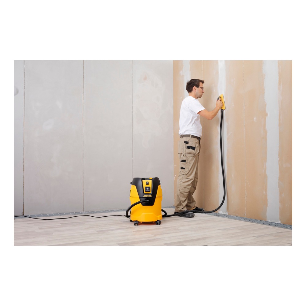 Person using a dust extractor beside a wall