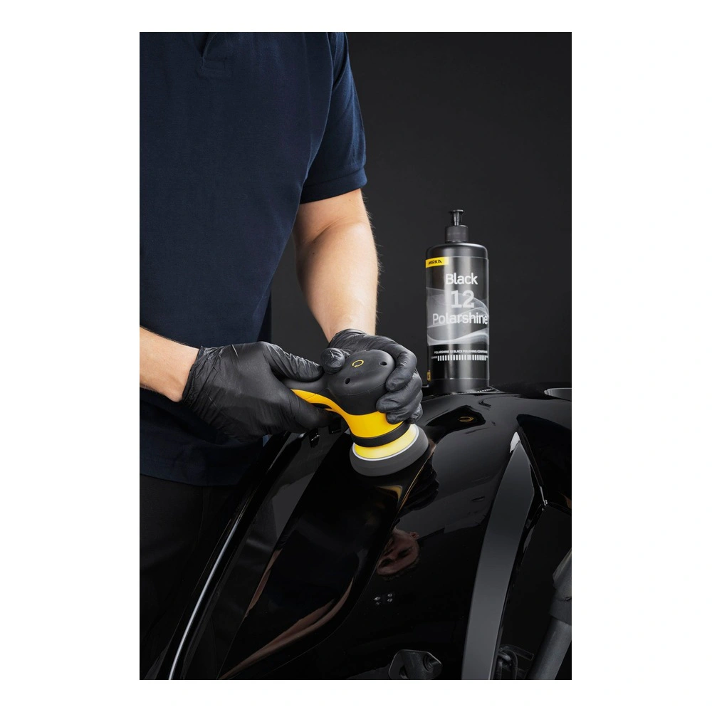 Person polishing glossy black surface, bottle behind